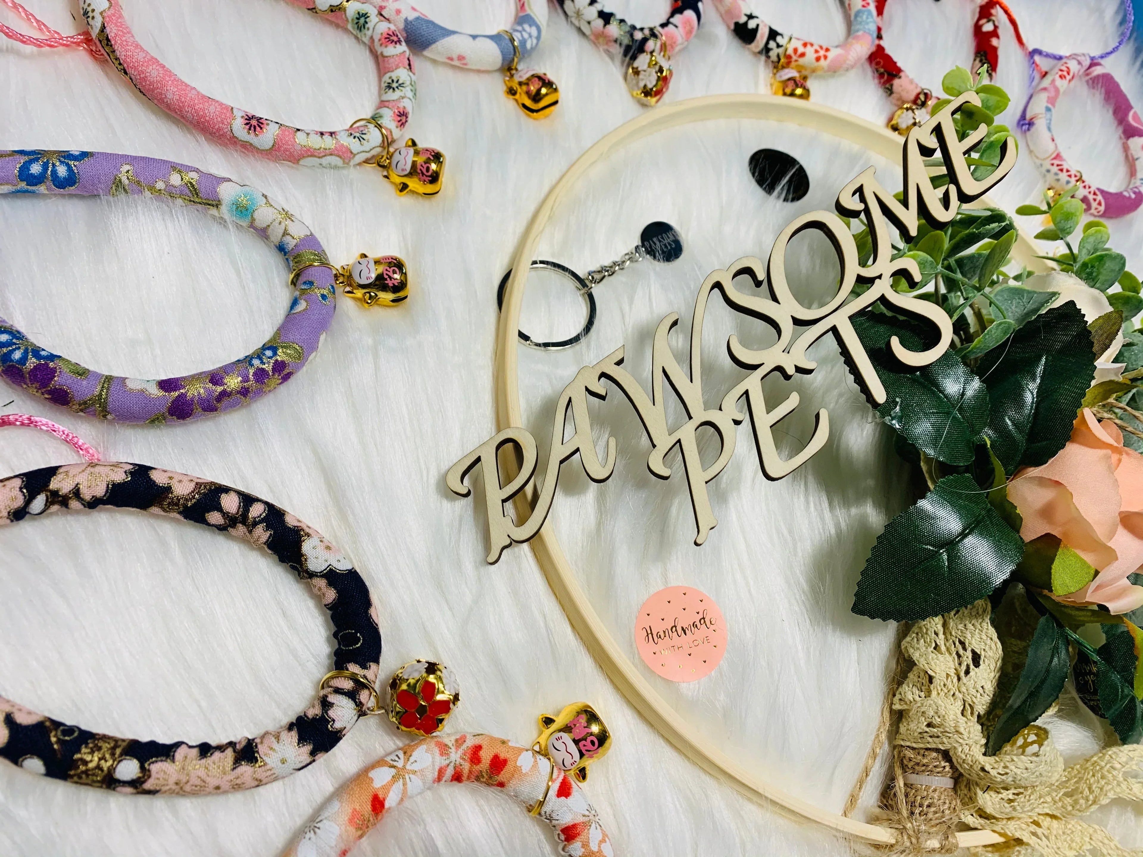 Colorful floral pet collars with cat charms on white fur background, paw print decor, and faux roses