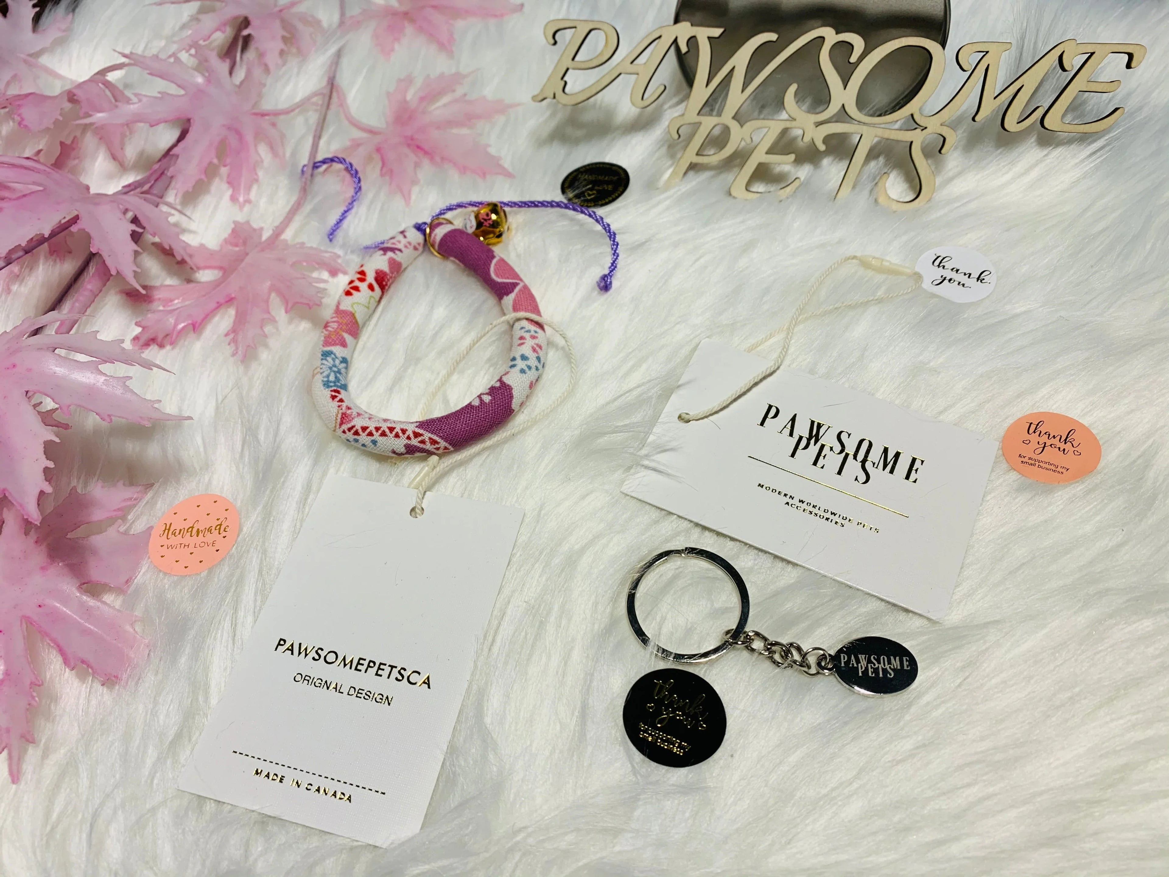 Colorful cat collar and pet keychain with Pawsome Pets tags on white faux fur background